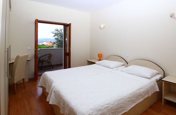 Un dormitorio con una cama doble, una silla, una mesita de noche y vistas al exterior a través de una puerta abierta.