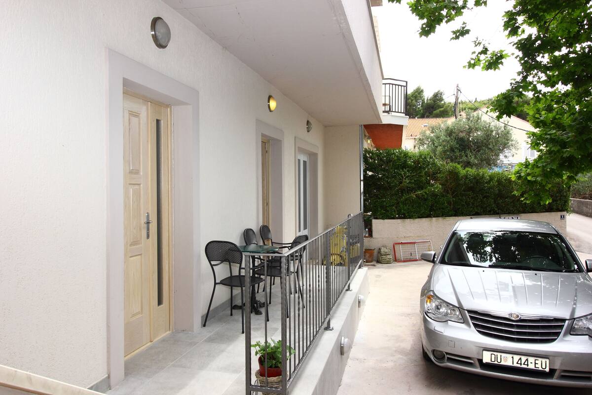 A residential building with a balcony, a parked car, and a door leading to a room.