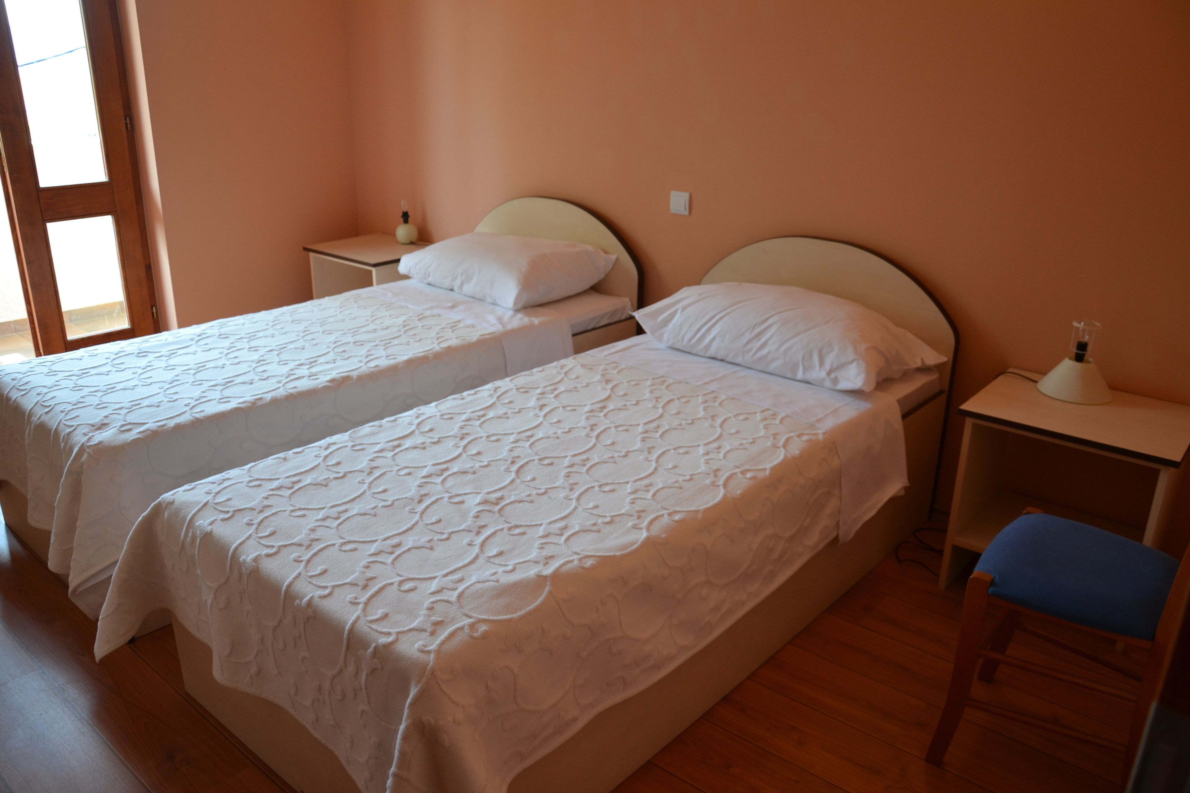 Une chambre avec deux lits, un plancher en bois, une table de chevet avec une lampe et une chaise.