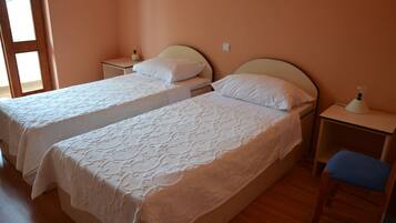 Una habitación con dos camas, suelo de madera, una mesita de noche con lámpara y una silla.