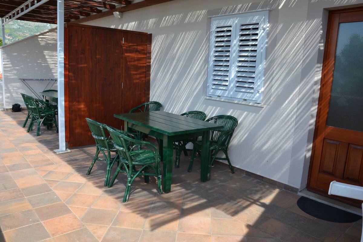 An outdoor patio with a wooden door, a window with shutters, and a table with chairs.