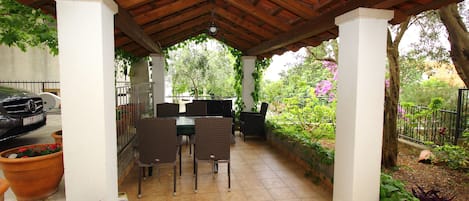 Un patio al aire libre con techo de madera, pilares blancos y una mesa con sillas.