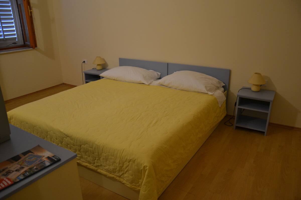 A neatly made bed with a yellow bedspread, two white pillows, and two bedside tables with lamps.