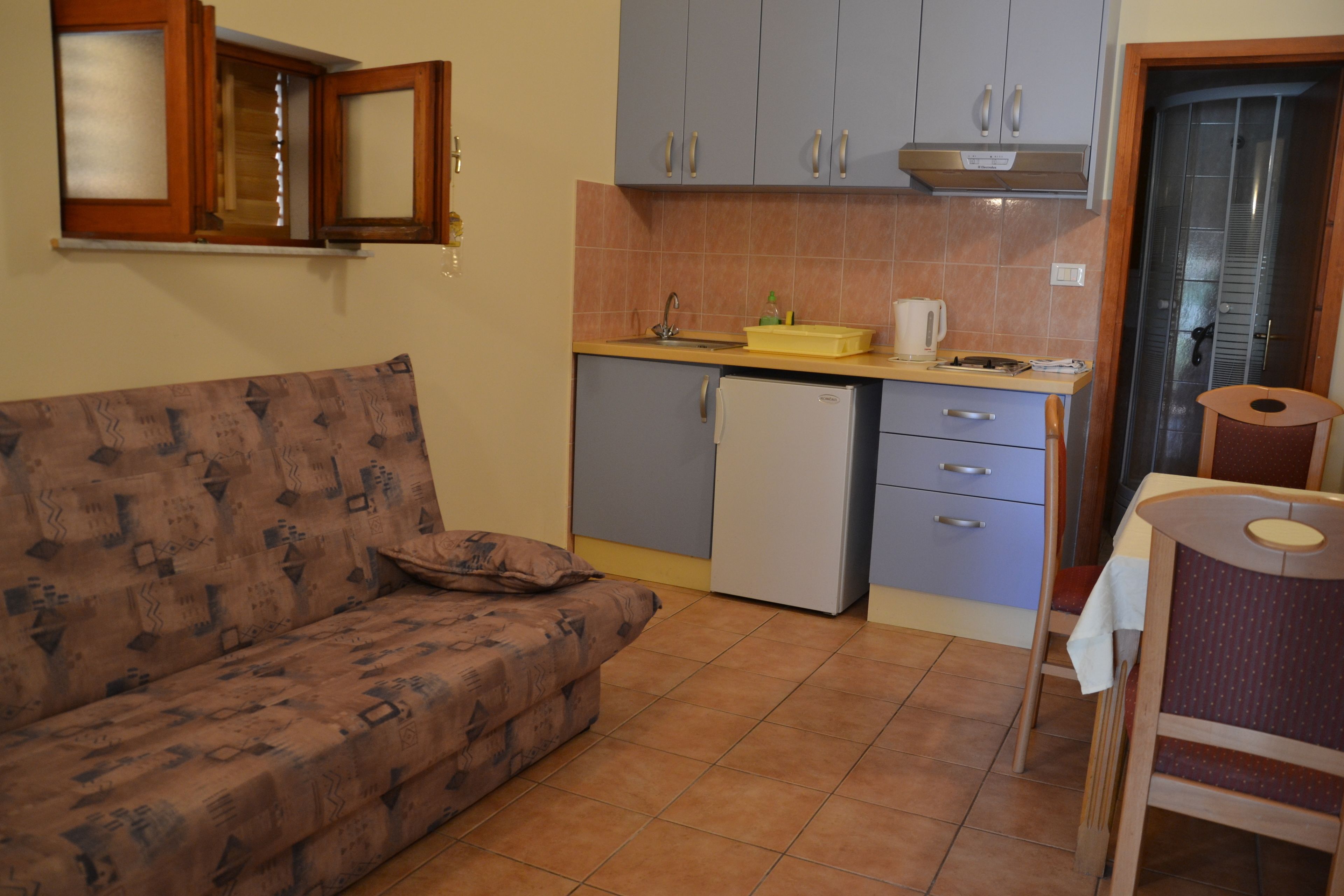 Una cocina compacta con refrigerador integrado, un lavamanos y un pequeño comedor con una silla.