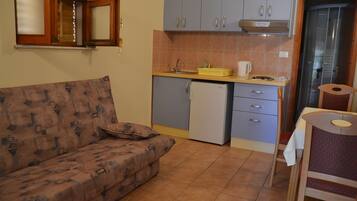 Una cocina compacta con refrigerador integrado, un lavamanos y un pequeño comedor con una silla.