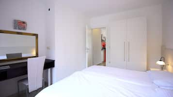A hotel room with a bed, a desk with a chair, a mirror, and a wardrobe.