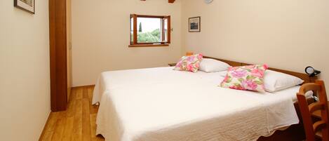 A bedroom with a wooden floor, a bed with white bedding, a window with a view of greenery, and a wooden ceiling.