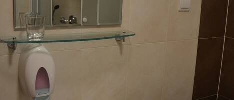 Un baño con un lavabo blanco, un estante de vidrio, un espejo y una toalla colgada en la pared.
