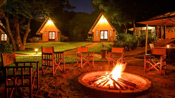 A campsite with two wooden cabins, a fire pit, and outdoor seating. - Ursula's Homestead (Victoria Falls)