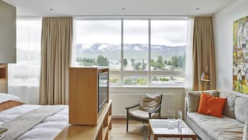 A hotel room with a bed, a sofa, a TV, and a large window with a mountain view.