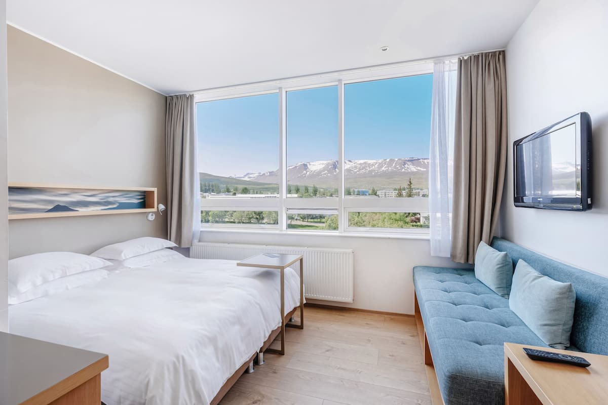 Una habitación de hotel con un ventanal grande, una cama, un sofá y un televisor.