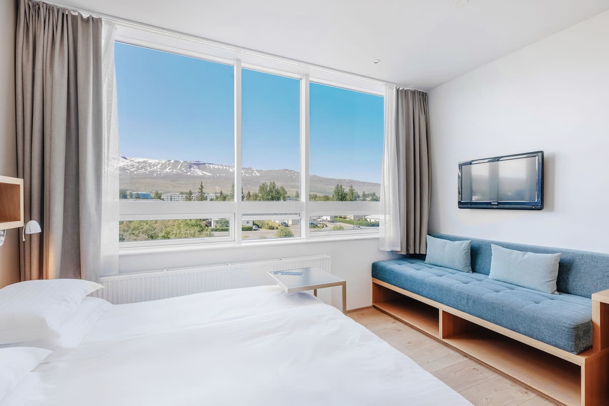 Una habitación de hotel con un ventanal grande, una cama, un sofá y un televisor en la pared.