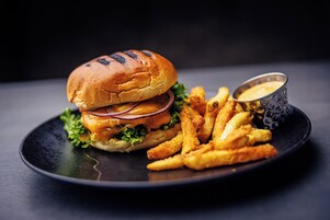 Una hamburguesa con papas fritas y una salsa para mojar, sobre un plato.