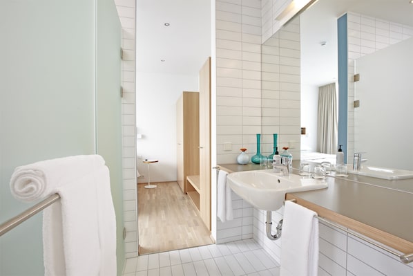 A modern bathroom with a large mirror, white tiles, and a wooden vanity. - Akureyri - Berjaya Iceland Hotels (Akureyri)