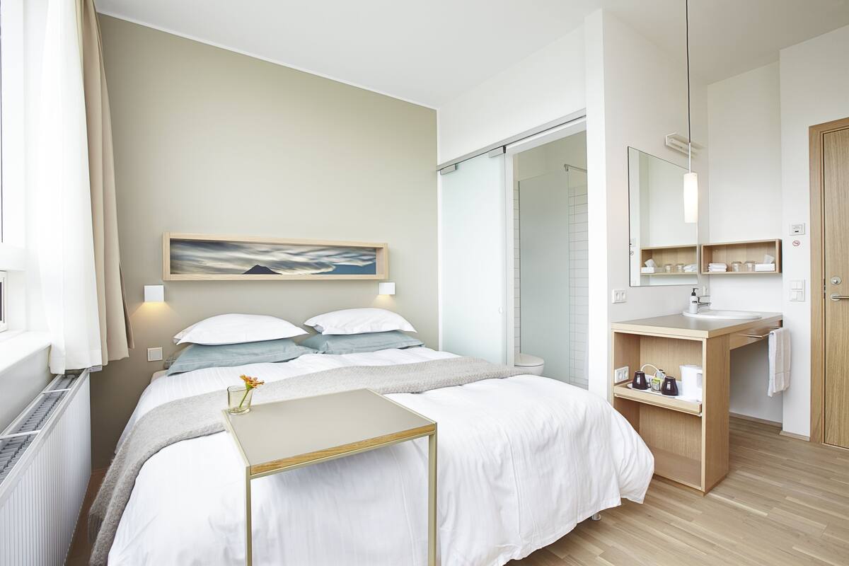 Une chambre d’hôtel moderne équipée d’un lit, d’une table de chevet et d’une salle de bain avec un lavabo et un miroir.