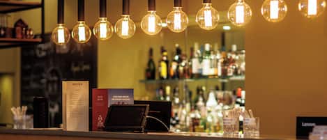 A bar area with hanging pendant lights, a counter with a menu, and shelves stocked with bottles.