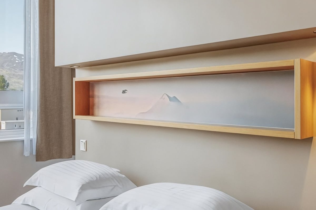 Een slaapkamer met een bed, een raam en een wandplank met een schilderij.