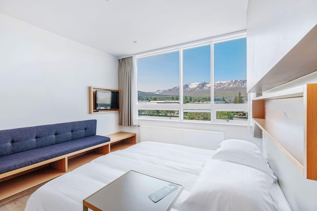 Una habitación de hotel moderna con un ventanal grande, una cama, un sofá y una mesita.
