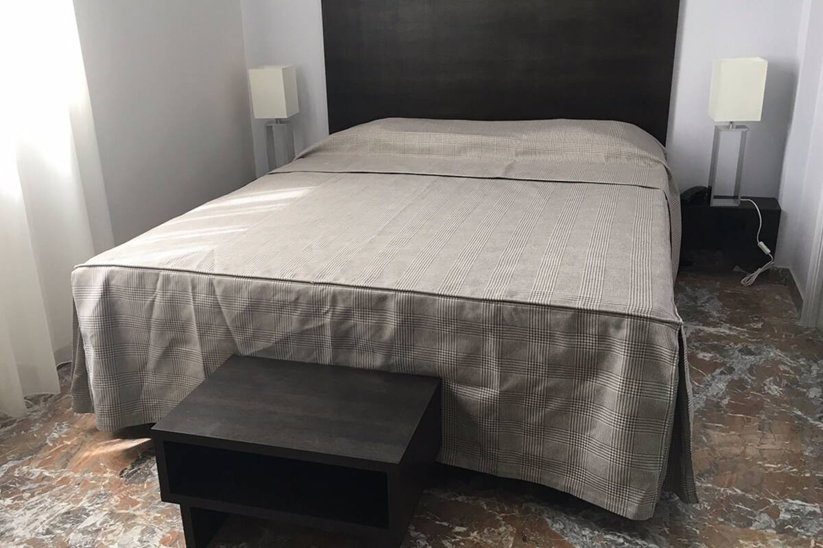 A neatly made bed with a checkered bedspread, a bedside table, and two wall-mounted lamps.