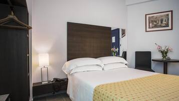 A hotel room with a bed, bedside table, lamp, and a small table with flowers.