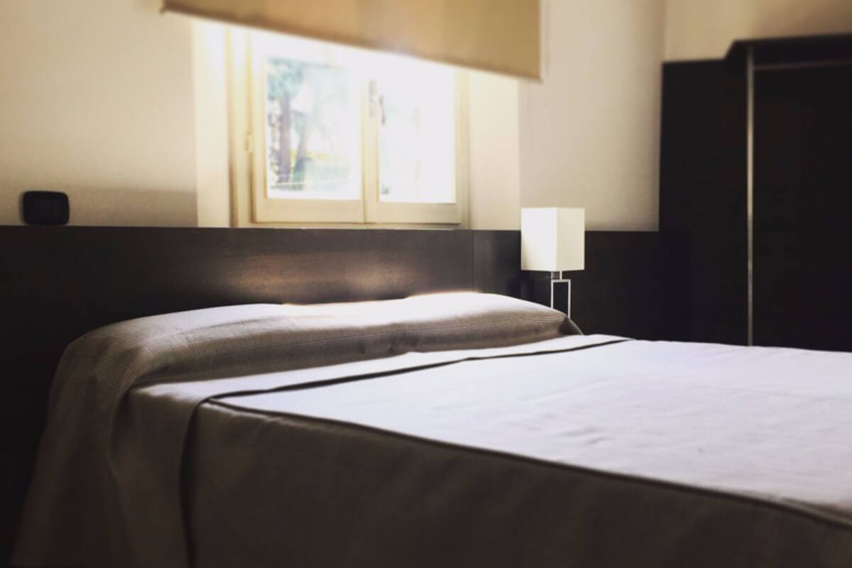 A hotel room with two beds, a window, a nightstand, and a wardrobe.