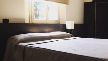 A hotel room with two beds, a window, a nightstand, and a wardrobe.