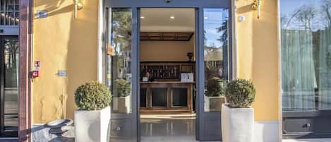 A hotel entrance with a reception desk, a door with a glass panel, and two potted plants.
