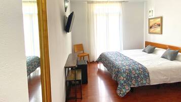 A hotel room with a bed, a desk, a chair, and a painting on the wall.