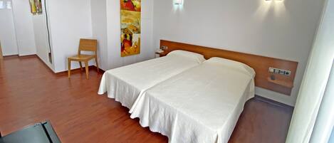 A hotel room with two beds, a wooden chair, a painting on the wall, and a nightstand with a phone.