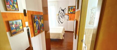 A hallway with wooden flooring, white walls, and several paintings.
