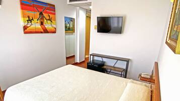 Ein Hotelzimmer mit einem Bett, einem an der Wand befestigten Fernseher und zwei Bildern an den Wänden.