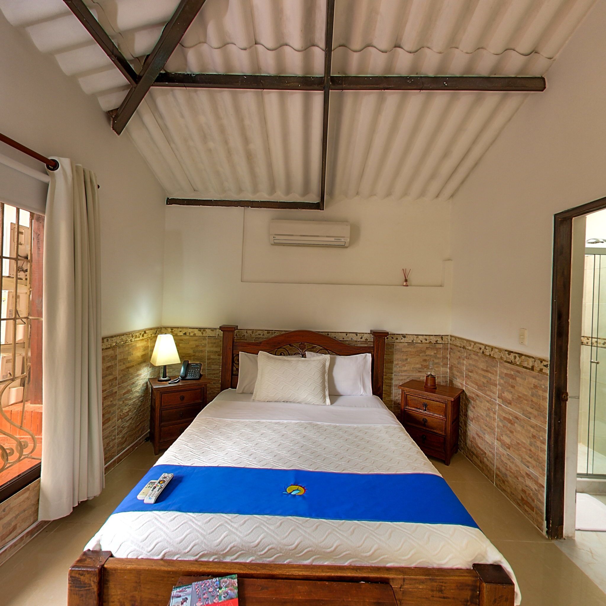 A hotel room with a bed, a nightstand with a lamp, a telephone, and a window with curtains.