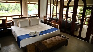 Une chambre spacieuse avec un grand lit, un banc en bois et une vue sur une piscine et la verdure environnante.