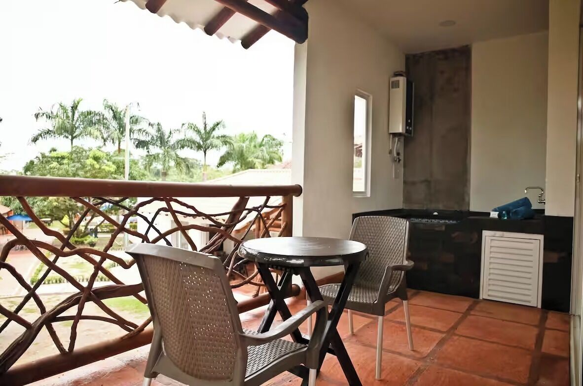 Un balcon avec des fauteuils en osier, une petite table ronde et un coin cuisine doté d’un plan de travail noir et de placards blancs.