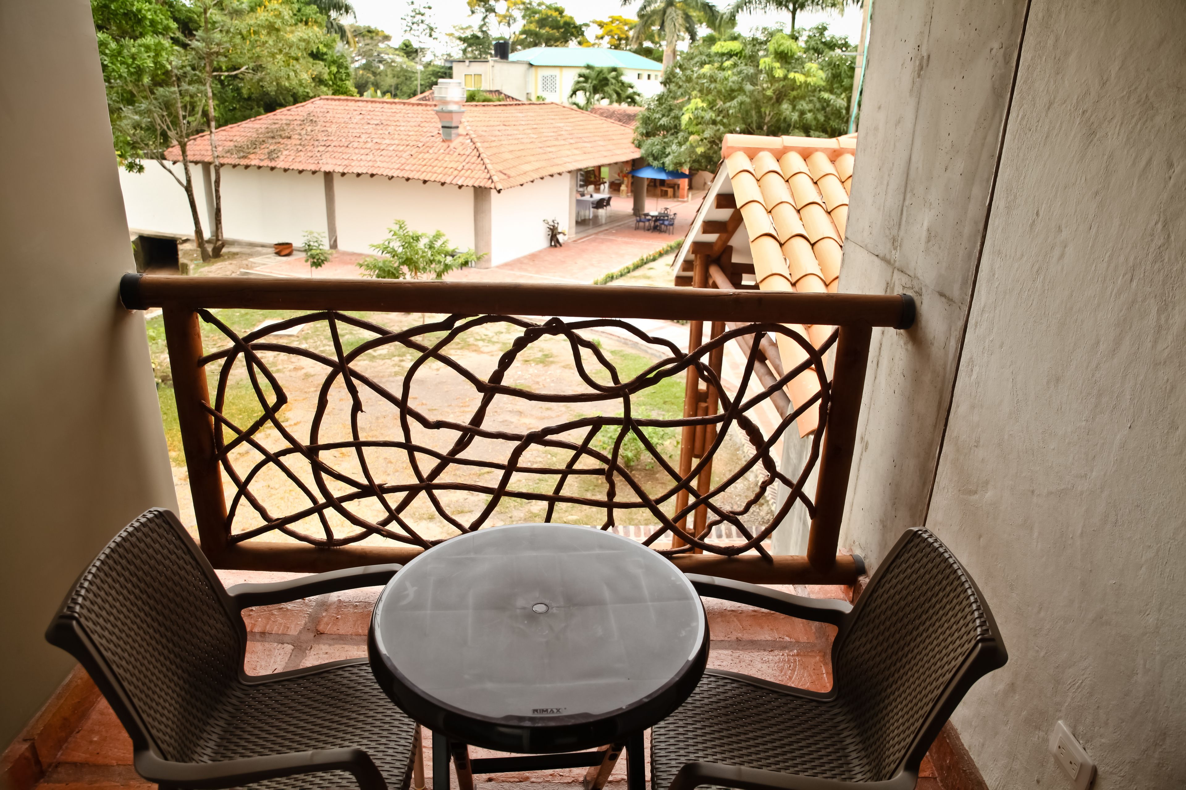 A balcony with a table and two chairs, overlooking a garden and buildings.