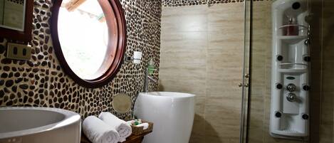 A bathroom with a stone wall, a round mirror, a large bathtub, and a shower area.