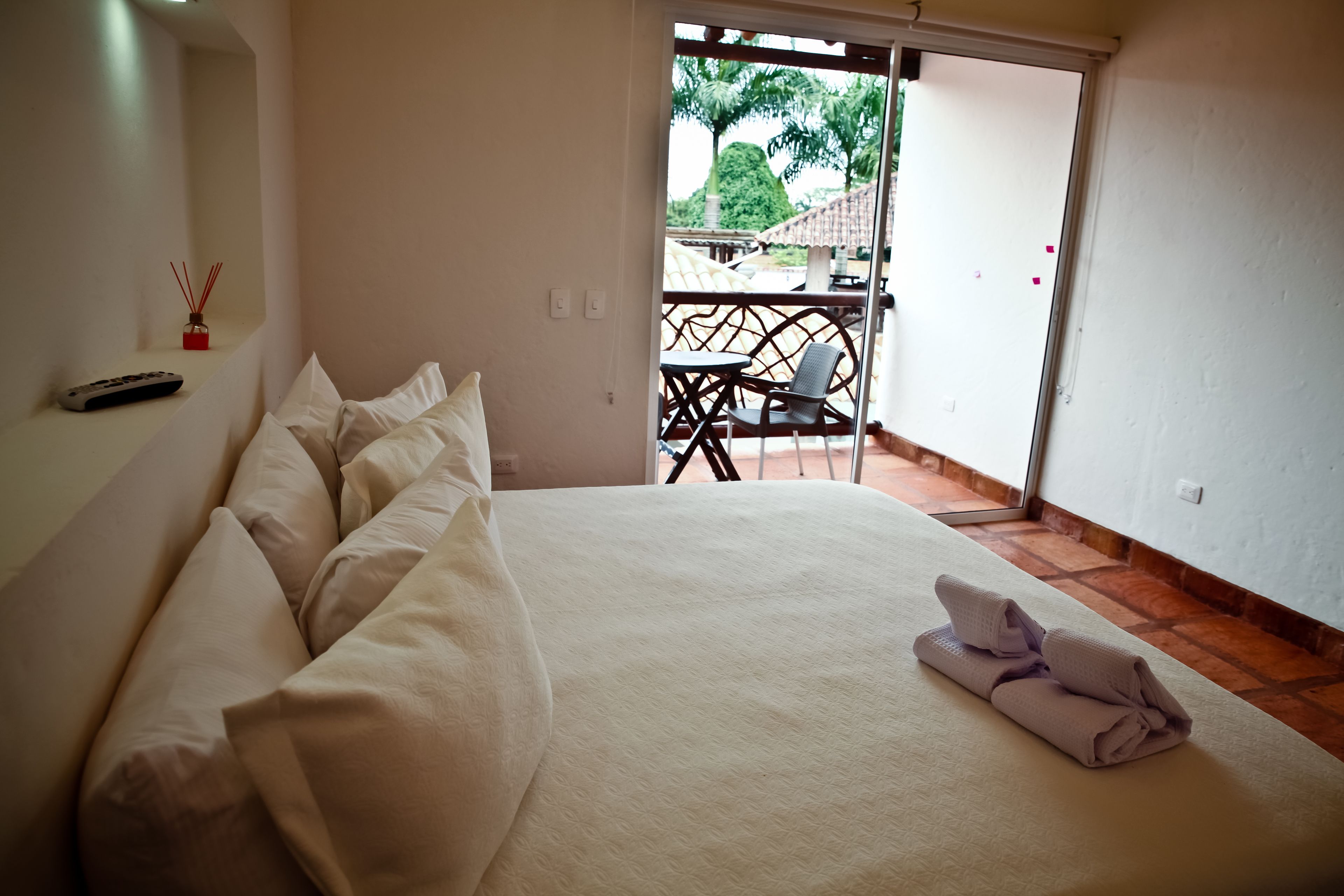 Une chambre d’hôtel avec un lit, une télécommande et un balcon équipé d’une table et de chaises.