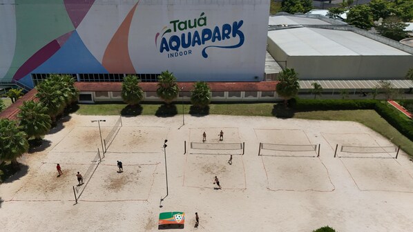 An indoor sports court with multiple volleyball nets, palm trees, and a large building with the sign "Tauá Aquapark Indoor". - Tauá Resort Atibaia (Atibaia)