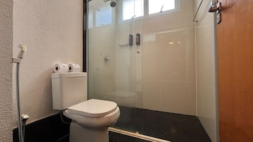 Casa de banho com sanita, cabine de duche em vidro e barra para toalhas.