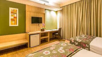 A hotel room with a desk, chair, two beds, a small refrigerator, and a TV.