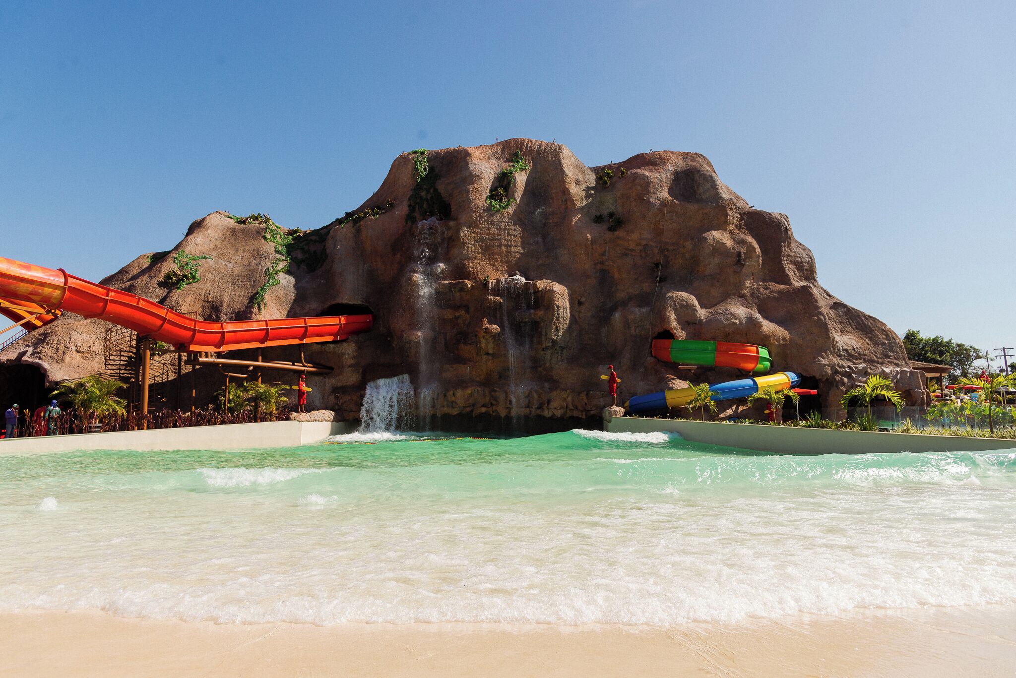 Un parque acuático con una gran formación rocosa, toboganes de agua y una playa de arena.