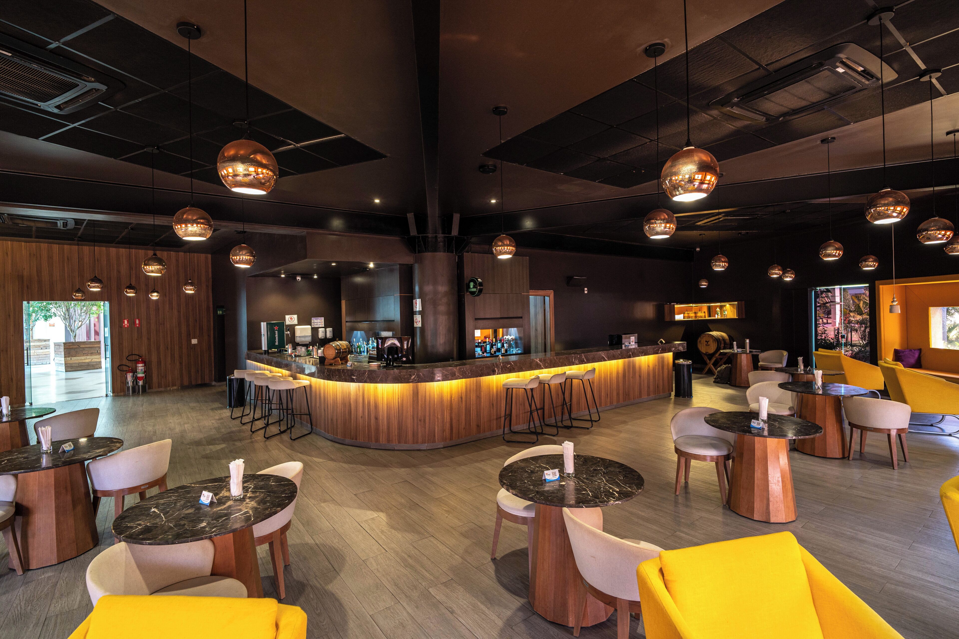 A modern bar area with a curved counter, multiple seating options including round tables and bar stools, and pendant lighting.