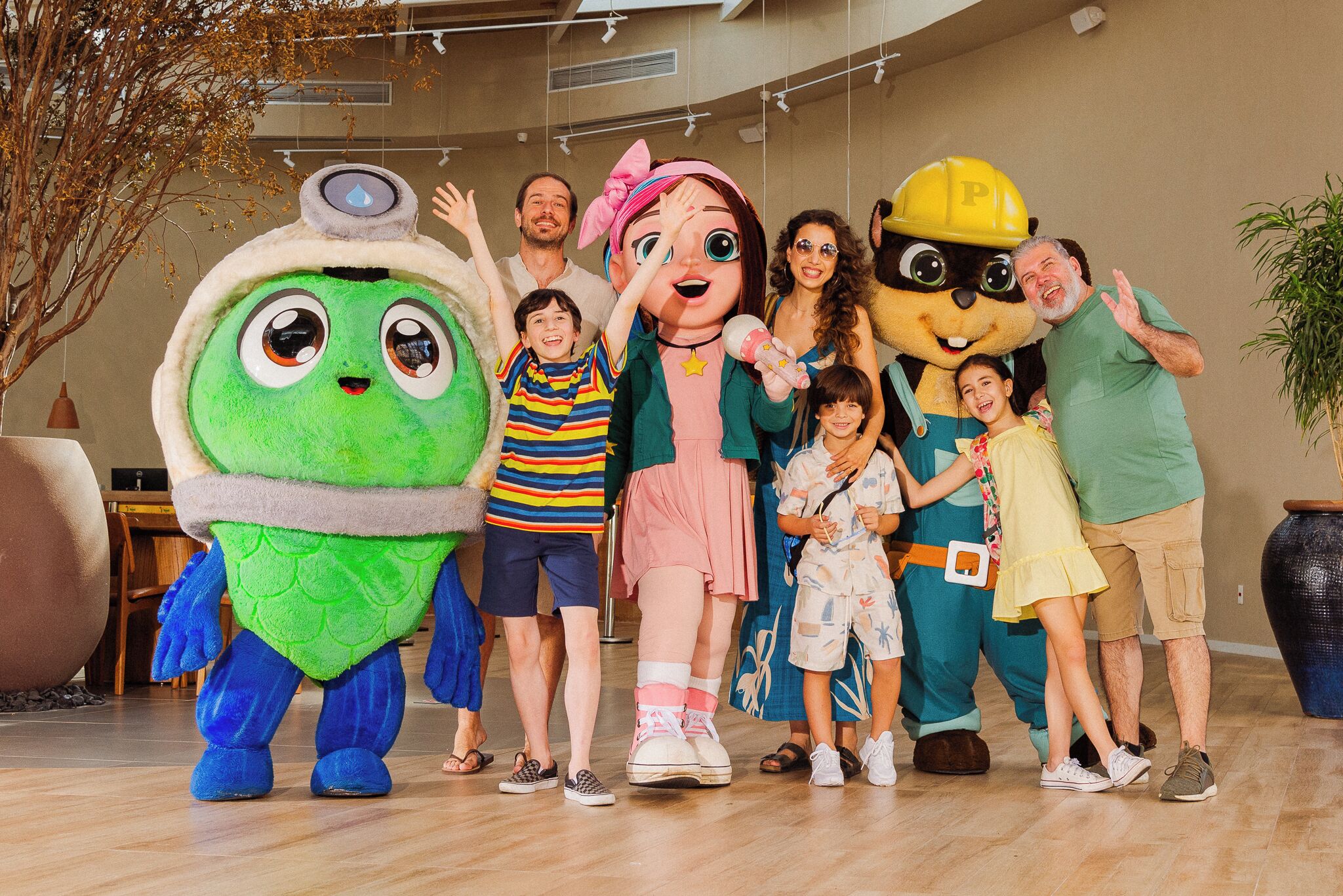 A group of people posing with large mascot characters in a spacious indoor area with a high ceiling and modern lighting.