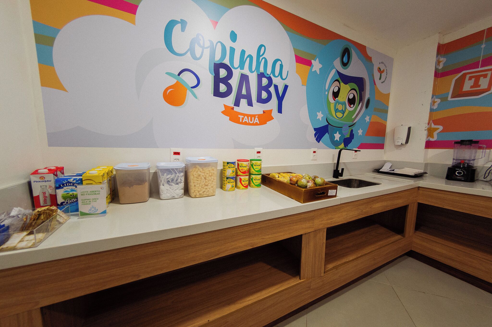 A kitchen counter with baby food products and a colorful mural with the text 'Copinha Baby.'