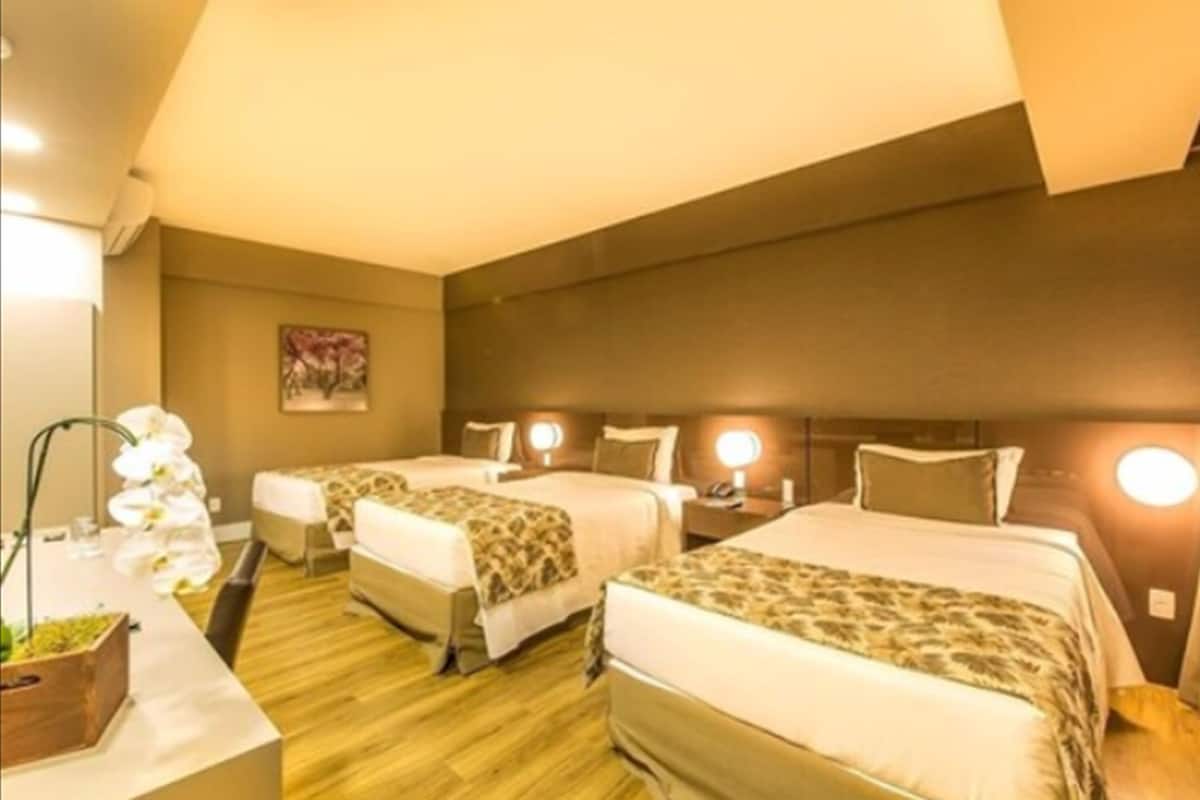 A hotel room with two beds, a wooden floor, a desk with a lamp, and a painting on the wall.