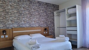 Una cama bien tendida con sábanas y toallas blancas, un cabecero de madera y una pared con diseño de piedra.