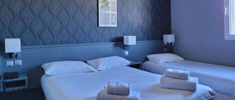 Une chambre d’hôtel avec deux lits, du linge de lit blanc et des serviettes. On y trouve des tables de chevet avec des lampes et une œuvre d’art accrochée au mur.