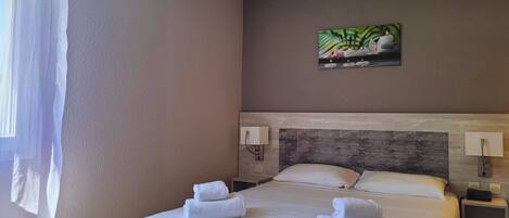 Habitación de hotel con una cama grande, dos mesitas de noche, un cabecero y un cuadro en la pared.