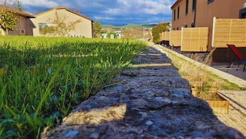 Un sendero bordeado de césped y una pared de piedra que conduce a edificios, con un cielo despejado al fondo.