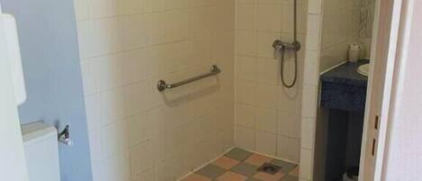 Un baño con inodoro, ducha con barra de apoyo y lavamanos.